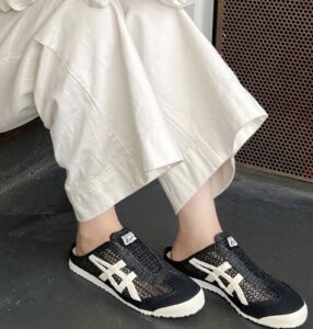WhatsApp_Image_2024-10-03_at_15.09.58 | UAE SPORT STORE Person wearing black patterned sneakers with white stripes, standing on a dark floor, beige wide-leg pants draped around the ankles.