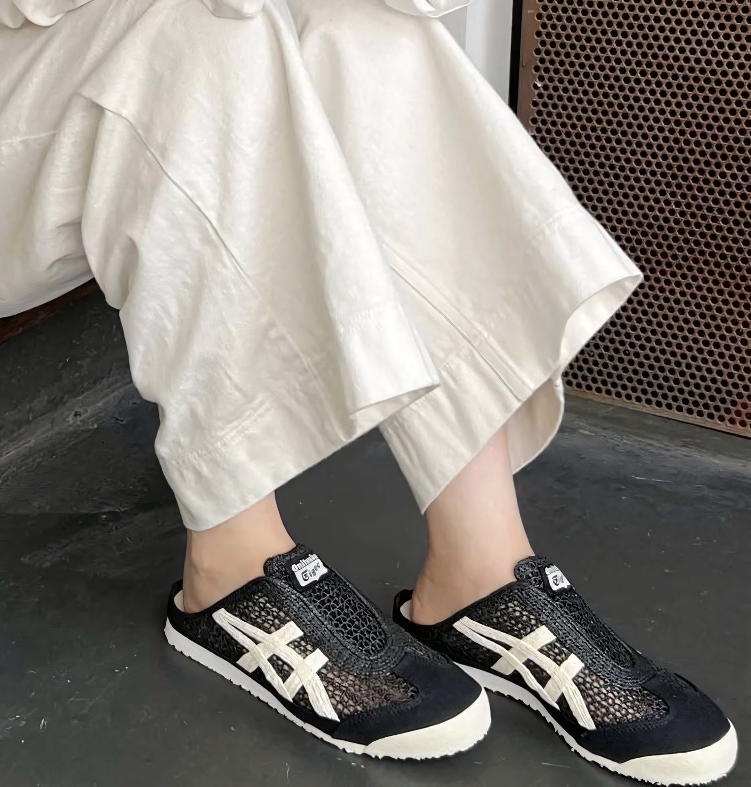 WhatsApp_Image_2024-10-03_at_15.09.58 | UAE SPORT STORE Person wearing black patterned sneakers with white stripes, standing on a dark floor, beige wide-leg pants draped around the ankles.