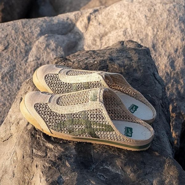 Two beige woven slip‑on shoes resting on a rocky surface outdoors