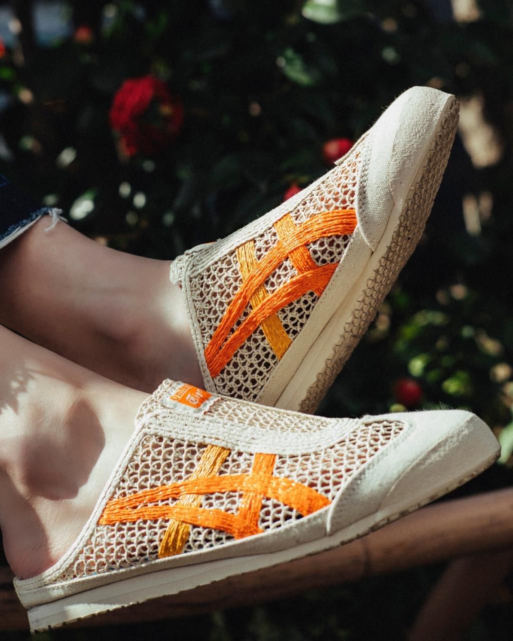 WhatsApp_Image_2024-10-04_at_12.40.27 | UAE SPORT STORE Beige woven slip-on sneakers with bright orange cross straps resting on a wooden railing.