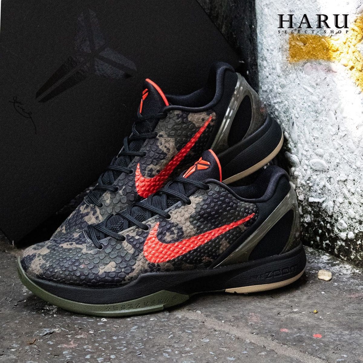 Black camouflage Nike basketball shoes with red-orange Swoosh resting on a curb, HARU logo in the top-right corner.