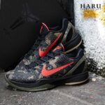 Black camouflage Nike basketball shoes with red-orange Swoosh resting on a curb, HARU logo in the top-right corner.