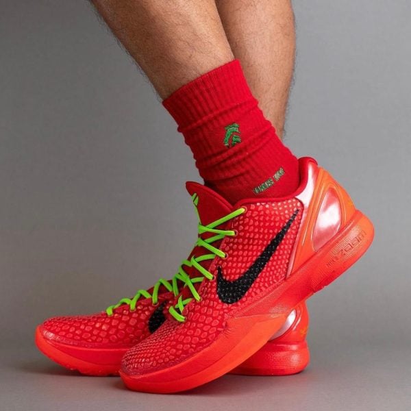 Red athletic sneakers with neon green laces, worn with matching red socks and a black Nike swoosh showing on the side.