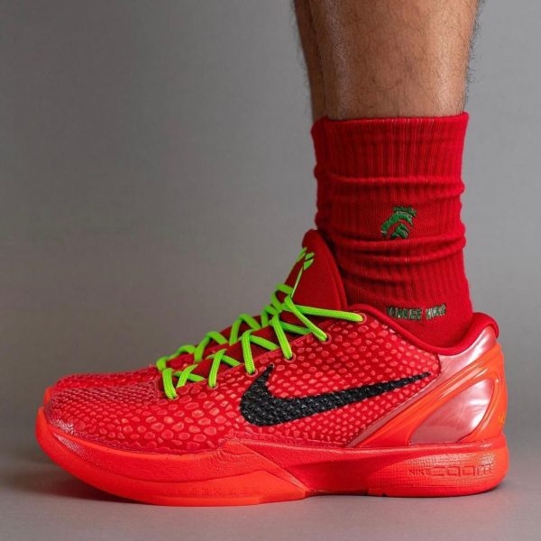 Red Nike training shoe with bright green laces worn with a red sock against a gray backdrop.