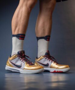 Athlete wearing gold Nike basketball shoes with red laces and white socks on a blue floor.