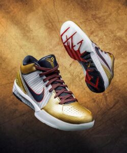 Gold and white basketball sneakers with red laces and a dark tongue, set against a textured bronze backdrop.