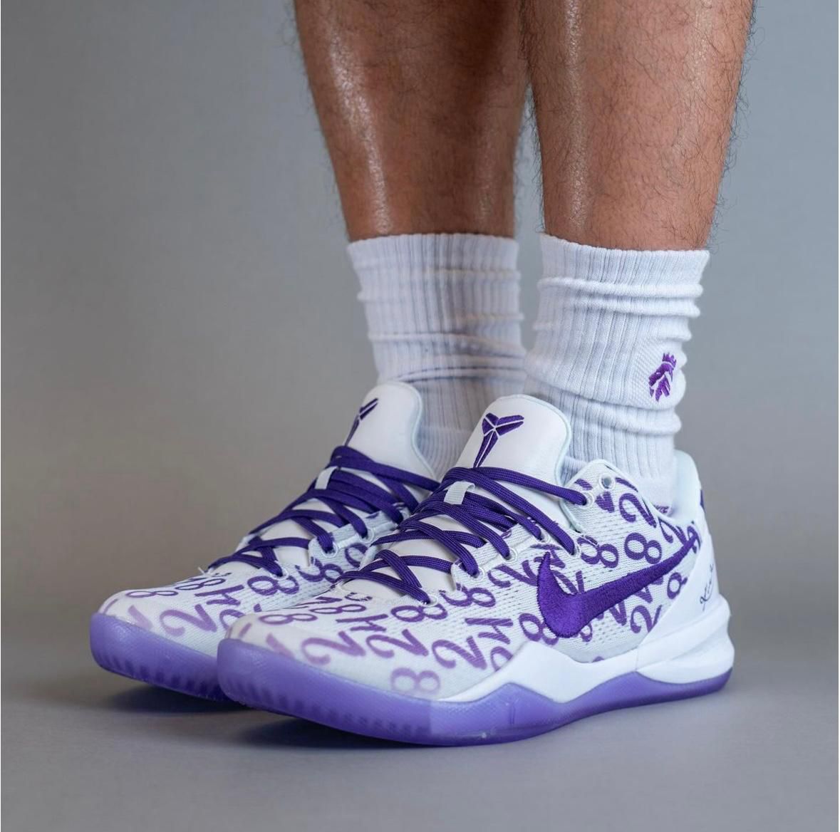 WhatsApp_Image_2024-10-09_at_12.23.33 White and purple Nike basketball sneakers with a purple pattern and matching laces, worn with white crew socks.