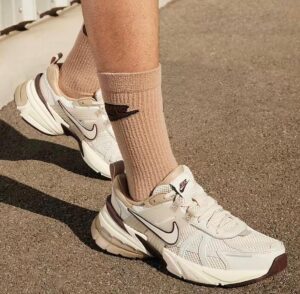 Close-up of beige and white Nike running shoes on a sandy surface, with matching tan socks visible by the ankles.