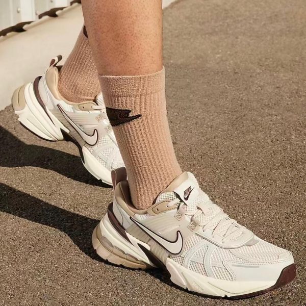 Close-up of beige and white Nike running shoes on a sandy surface, with matching tan socks visible by the ankles.