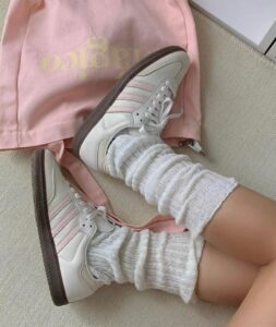 WhatsApp_Image_2024-10-12_at_10.42.25 | UAE SPORT STORE White sneakers with pink accents and fluffy white socks resting on a beige surface beside a pale pink bag.