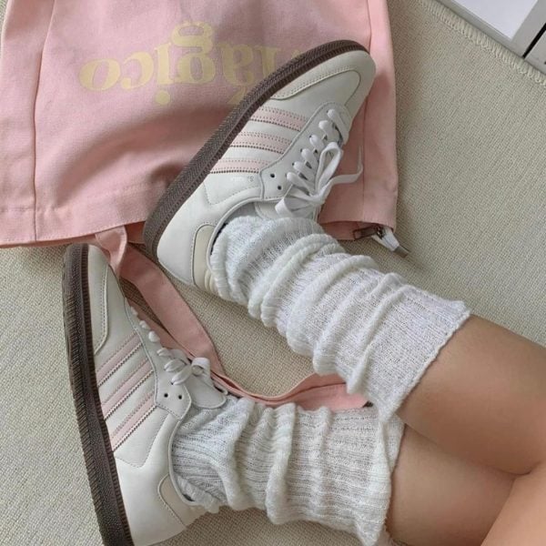 White sneakers with pink accents and fluffy white socks resting on a beige surface beside a pale pink bag.