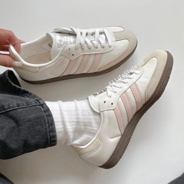 Pair of white sneakers with light pink side stripes, shown with white socks and jeans from a top-down angle (lifestyle photo).