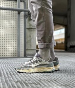 Side view of a gray Nike sneaker on a metal grate, with rolled gray jeans and matching socks in an urban setting (P-6000 visible).