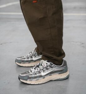 Person wearing brown pants and gray Nike sneakers standing on a concrete pavement.