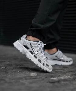 Grey and white Nike running sneakers with black swoosh on a dark pavement, worn with black joggers.