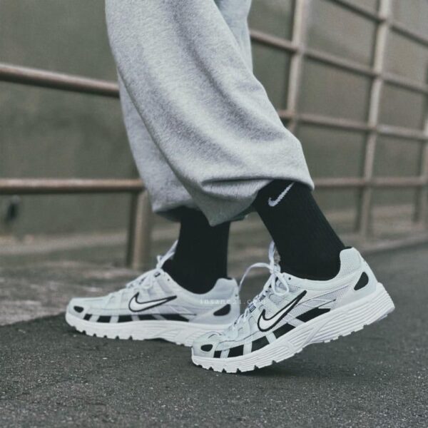 Close-up of white Nike running shoes worn with gray sweatpants and black socks on a sidewalk.