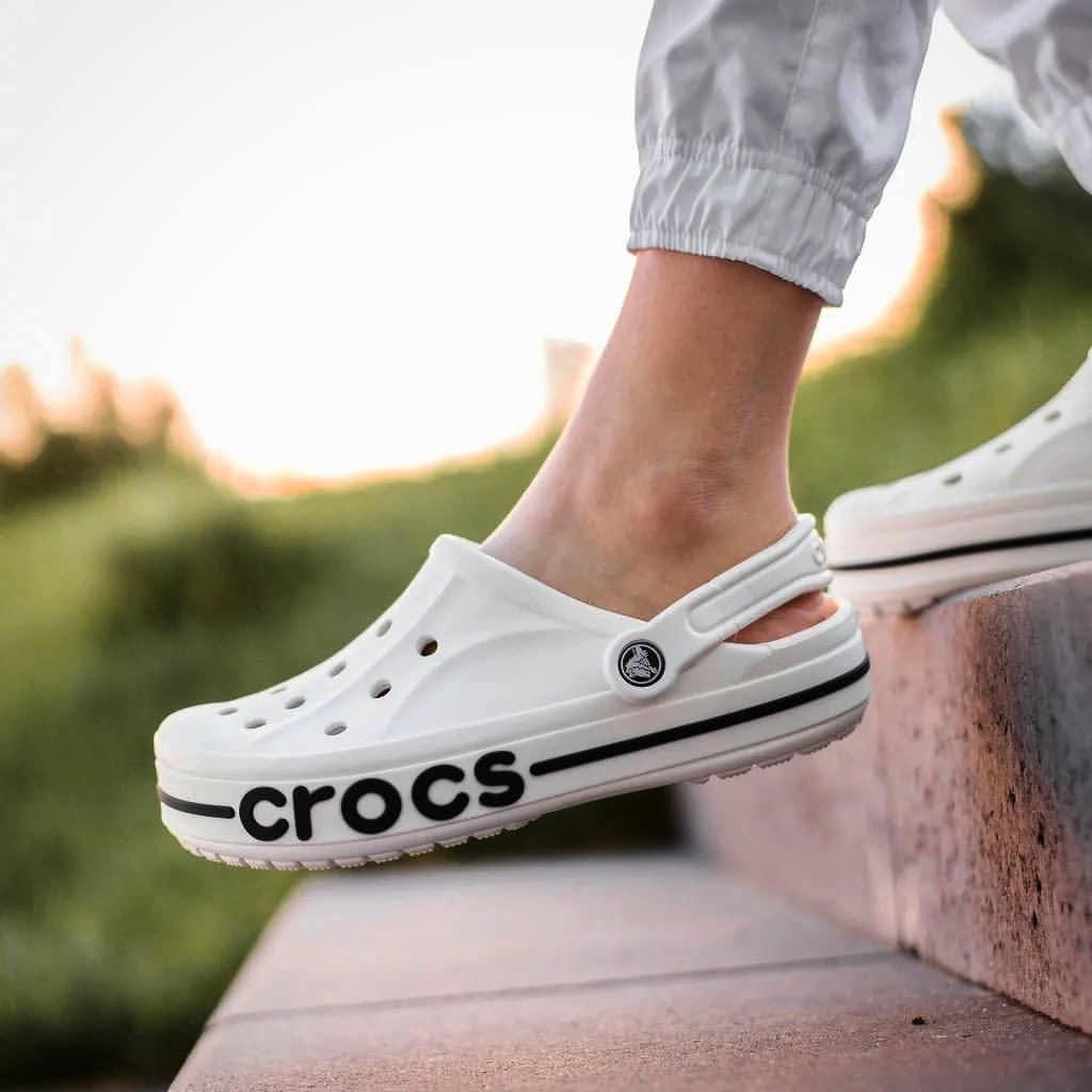 WhatsApp_Image_2024-10-18_at_11.29.21 | UAE SPORT STORE White Crocs clog with bold black 'CROCS' lettering along the sole, worn by a person stepping onto a concrete step outdoors.