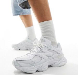 White chunky sneakers with laces, worn with white crew socks and denim shorts on a light background.