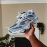 Hand holding a light blue New Balance sneaker indoors, showing the side with the large N logo