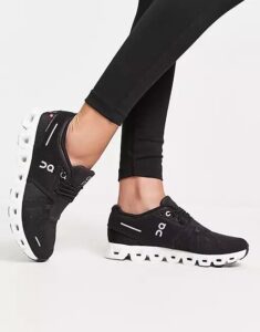 Black On running shoes with a white segmented sole, worn with black leggings on a white background.