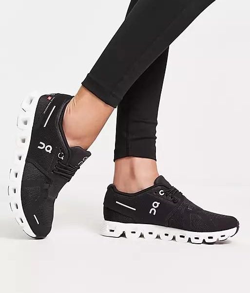 Black On running shoes with a white segmented sole, worn with black leggings on a white background.