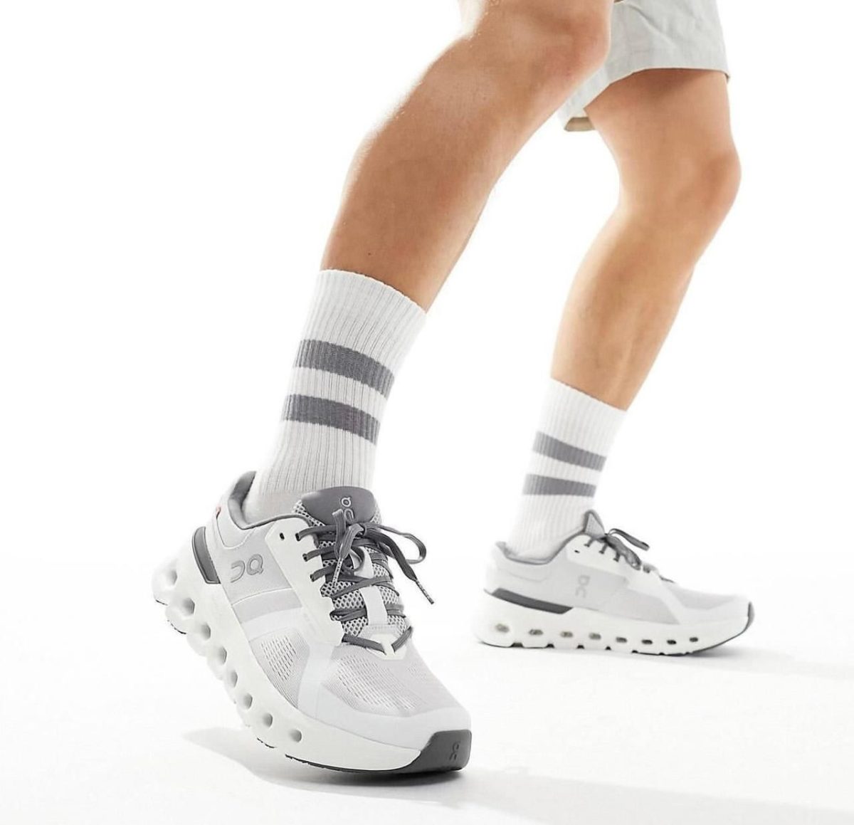 Person wearing white and gray running shoes with striped socks, mid-stride, on a white background