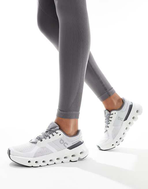 Close-up of a person wearing white athletic sneakers with a chunky sole and gray leggings on a white background.