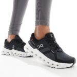 Black On Running sneakers with a chunky white sole, worn with gray leggings by a person standing.