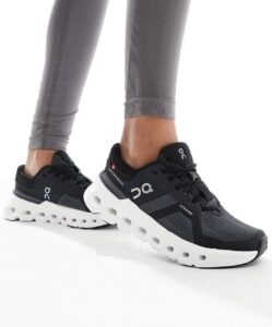 Black On Running sneakers with a chunky white sole, worn with gray leggings by a person standing.
