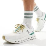 White athletic sneakers with green accents being worn over striped white socks with green bands, showcasing a chunky sole.