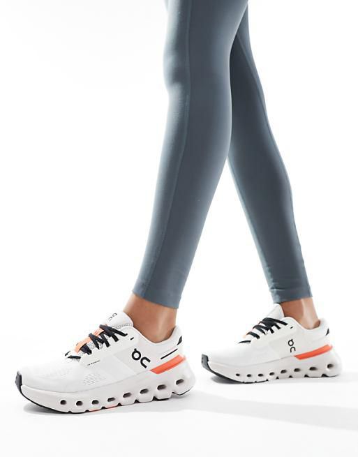 Person walking in white athletic sneakers with black laces and orange heel accents, wearing blue-gray leggings.