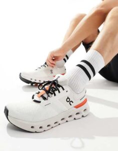 Close-up of a person tying white athletic sneakers with black laces and striped socks on a light floor.