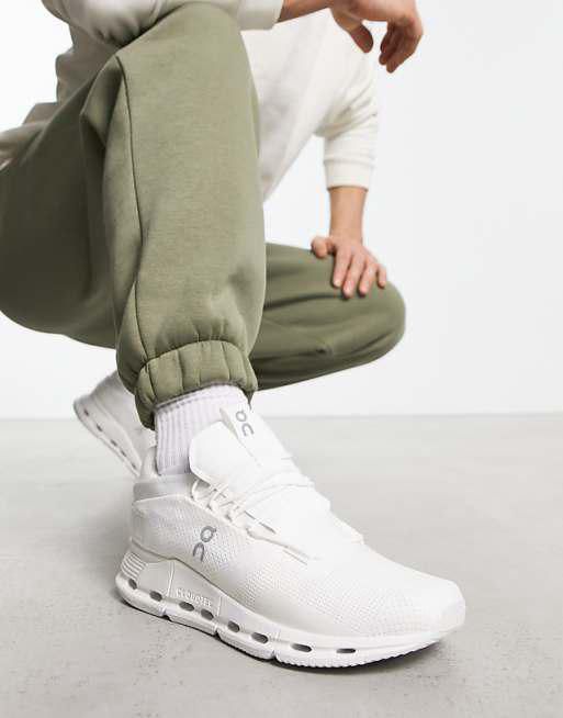 WhatsApp_Image_2024-11-06_at_10.52.37 | UAE SPORT STORE Close-up of a person wearing white athletic sneakers, olive joggers, and white socks, crouching on a light floor.