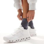 WhatsApp_Image_2024-11-06_at_10.52.38 | UAE SPORT STORE Person tying white athletic sneakers while wearing dark gray socks, close-up of lower legs.