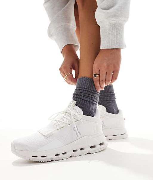 Person tying white athletic sneakers while wearing dark gray socks, close-up of lower legs.