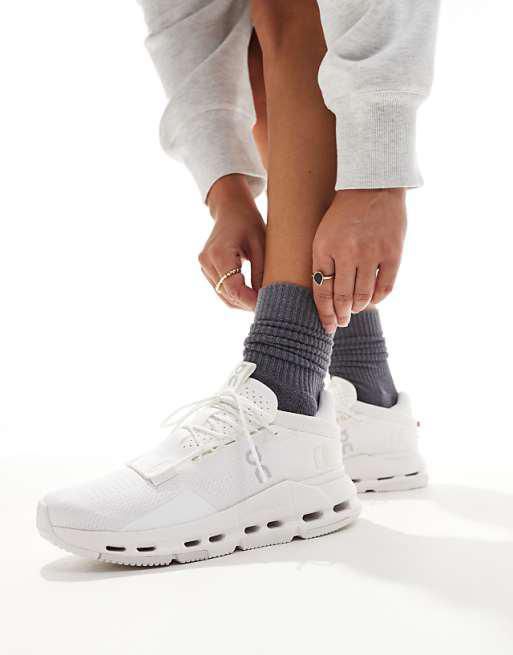 Person tying white athletic sneakers while wearing dark gray socks, close-up of lower legs.