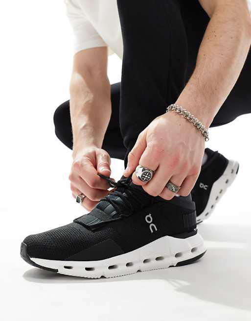 Person tying the laces of a black On running shoe with a white sole on a light background.