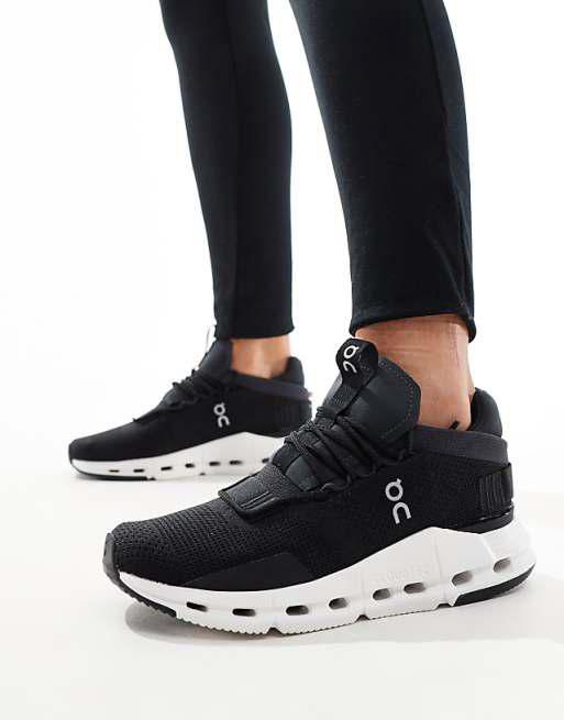 Black athletic sneakers with white chunky sole and On logo, worn with black leggings in a standing pose.