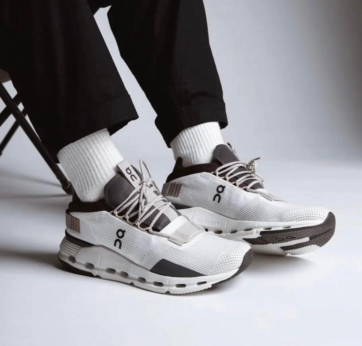 WhatsApp_Image_2024-11-08_at_10.45.42 White and gray On-brand running shoes on a person wearing white socks and black pants, standing on a light surface.
