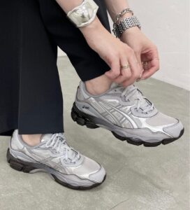 WhatsApp_Image_2024-11-08_at_11.04.47 | UAE SPORT STORE Person tying gray Asics running shoes, wearing multiple silver bracelets and rings, with black pants in a minimal setting.