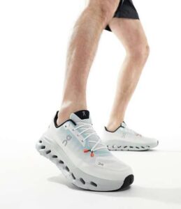 Runner wearing white On Cloud running shoes mid-stride against a white background.