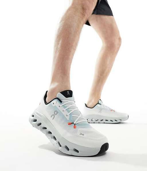Runner wearing white On Cloud running shoes mid-stride against a white background.