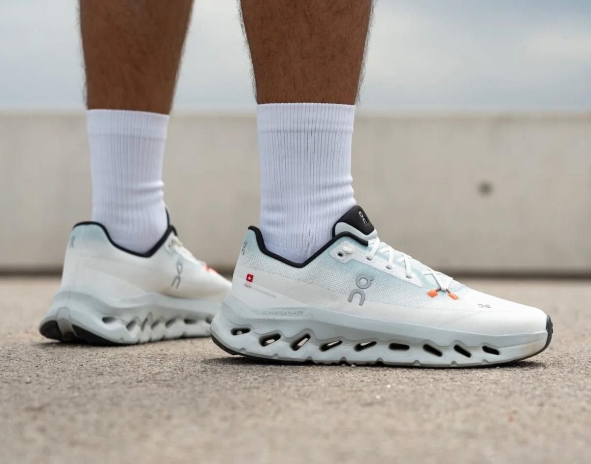 White athletic running shoes with white socks standing on a concrete surface, focus on the shoes' chunky sole.