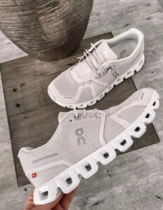 Pair of light gray On running shoes with thick, segmented white soles on a wooden surface, showing the brand logo on the side.