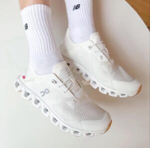 White running shoes with breathable mesh and chunky sole, worn with white ribbed socks.