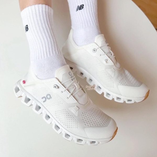 White running shoes with breathable mesh and chunky sole, worn with white ribbed socks.