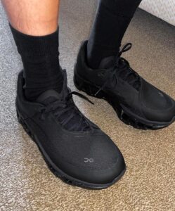 WhatsApp_Image_2024-11-12_at_14.02.52 | UAE SPORT STORE Person wearing black athletic sneakers and black socks standing on a carpeted floor, showcasing a chunky sole design.