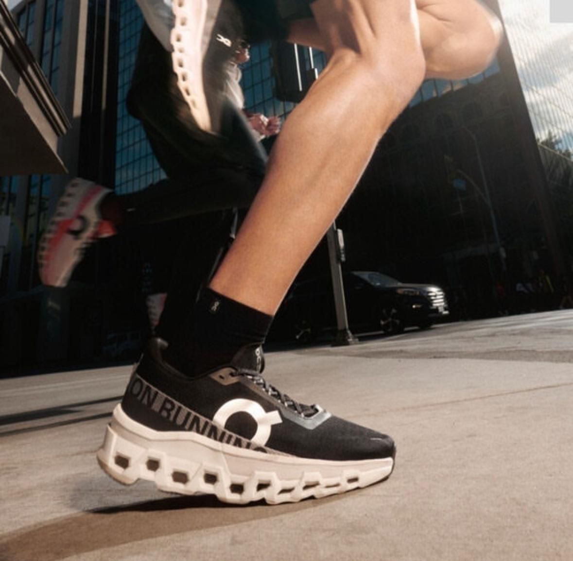 WhatsApp_Image_2024-11-13_at_13.44.19 | UAE SPORT STORE Close-up of a black ON Running sneaker with a chunky white sole on a city sidewalk.