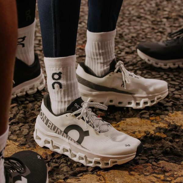 Pair of white On running trail shoes with chunky built-up midsoles and white socks on a rocky gravel path.