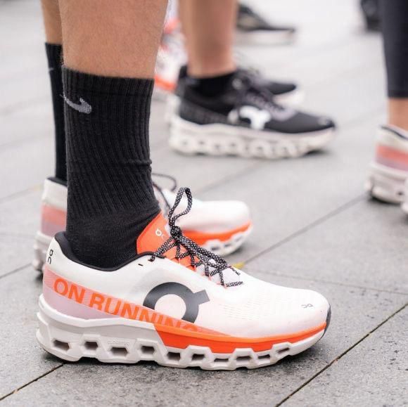 Athlete wearing white and orange On Running running shoes with black socks on a paved street, midfoot view focus on shoe design